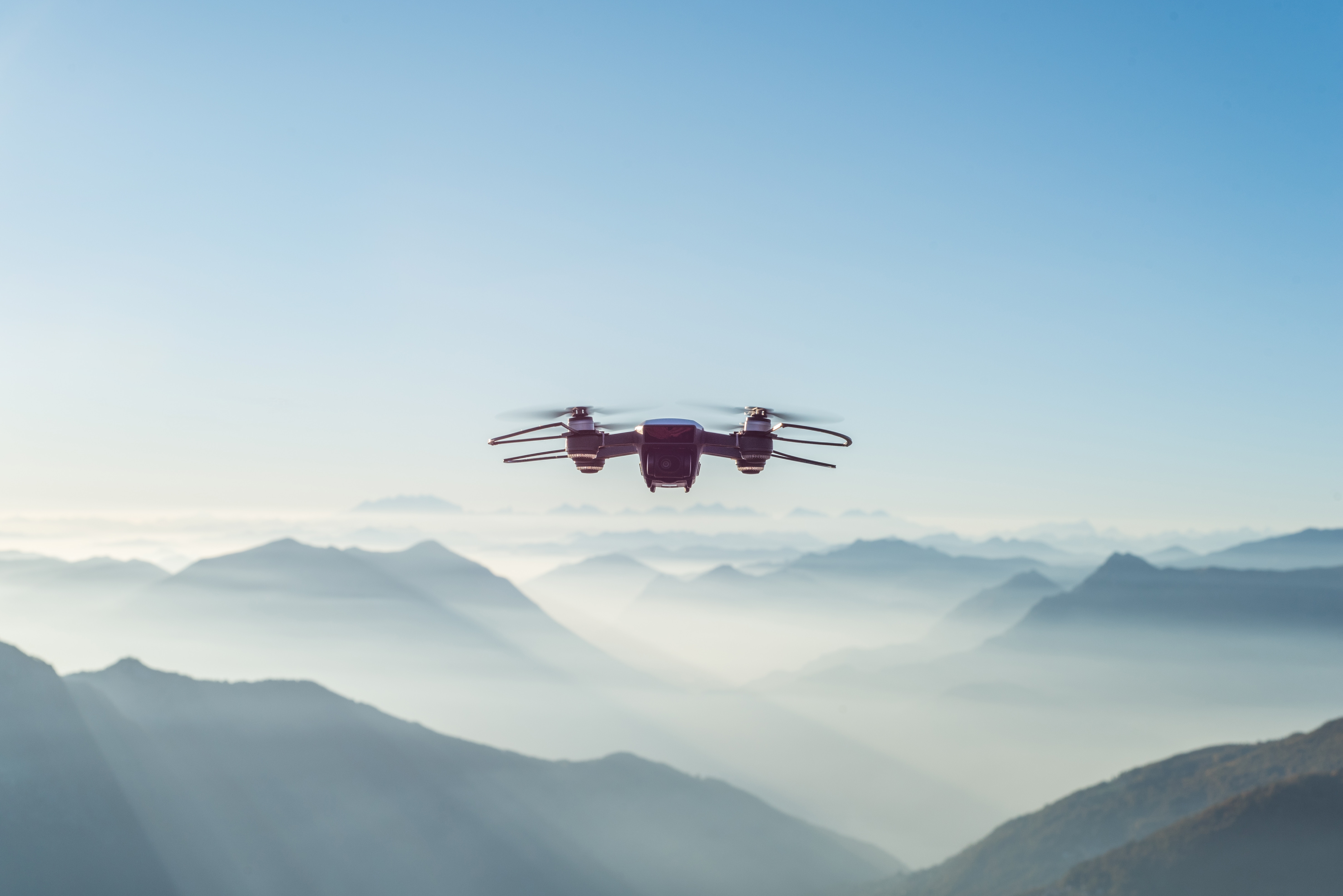 four propeller drone flying above the clouds in a mountain scape