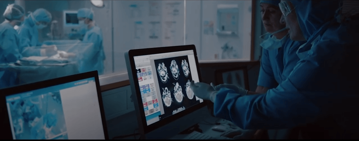 Doctors looking at an ultrasound on a screen while surgeons perform surgery in the background